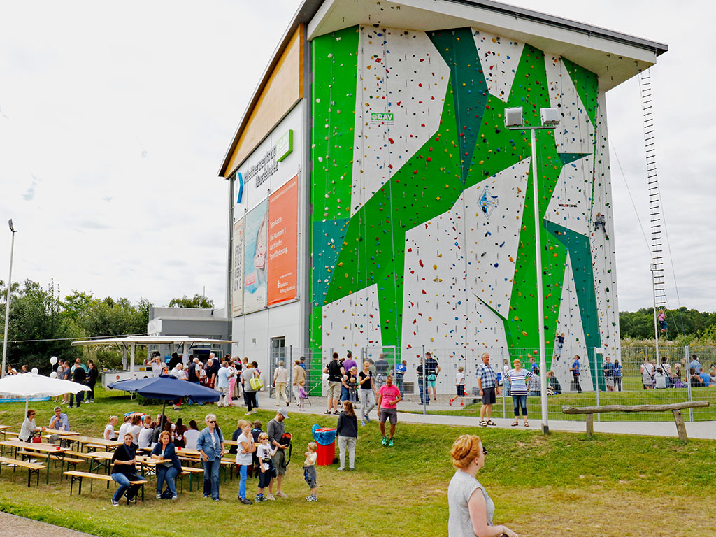 Besucher vor dem hohen Gebäude mit einer großen Kletterwand