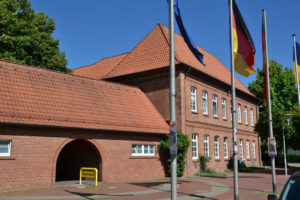 Großes altes Rathaus in Buchholz aus roten Mauersteinen und roten Dachziegeln mit Flaggen im Vordergrund