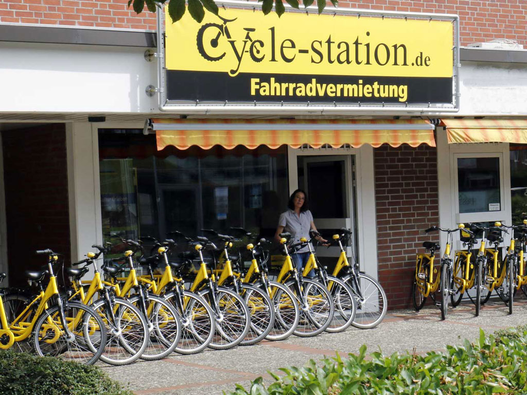 Fasade und Eingang der Cycle Station mit vielen gelben Leihfahrrädern