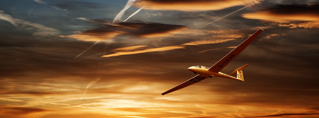 Ein Segelflugzeug fliegt unter leichten Wolken durch den roten Himmel