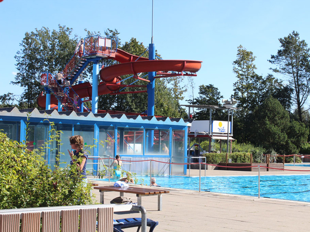 Blaues Wasser im Schwimmbecken mit einer großen roten Rutsche im Hintergrund