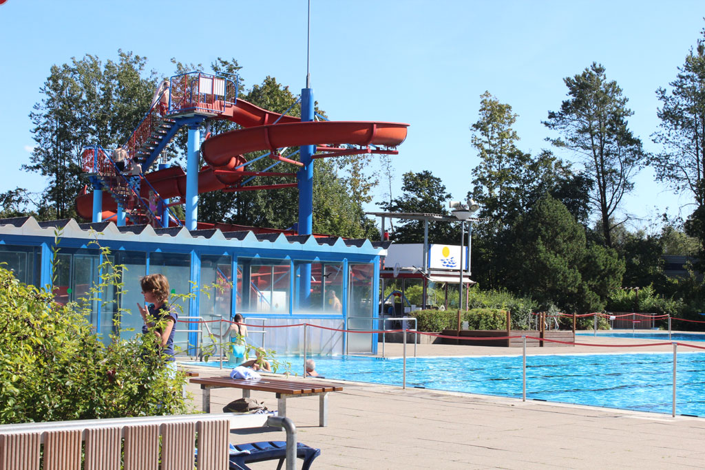 Blaues Wasser im Schwimmbecken mit einer großen roten Rutsche im Hintergrund