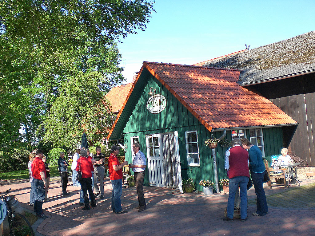 Besucher auf dem Bauernhof stehen vor dem kleinen grün-weißen Melkhus-Anbau mit rotem Pfannendach