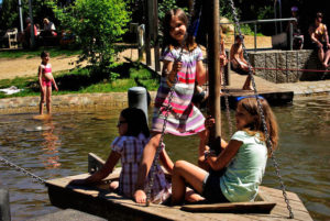 Drei Kinder schaukeln in einer Schiffschaukel über das Wasser