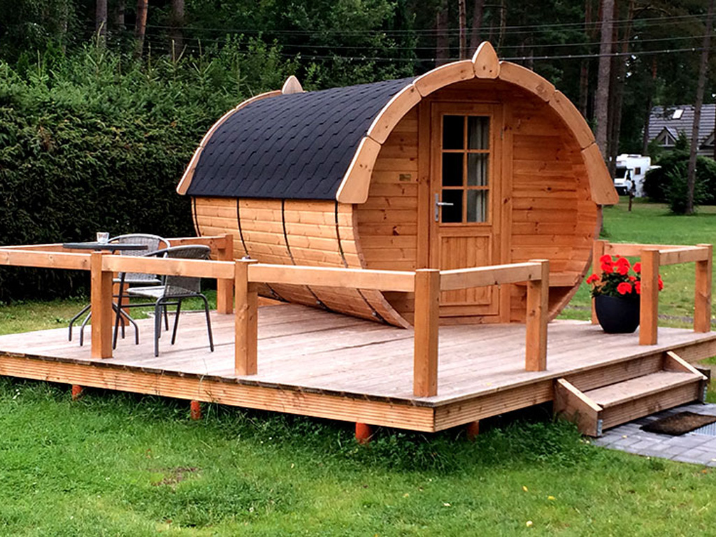 Ein kleines Ferienhaus aus Holz in Form eines Fasses mit Terrasse aus Holz und zwei Stühlen mit Tisch