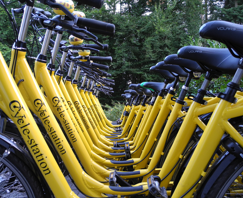 Fasade und Eingang der Cycle Station mit vielen gelben Leihfahrrädern